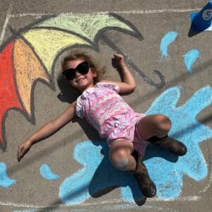 A Closeup look of a drawing on the concrete surface and a small girl laying on it.