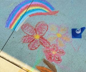 Chalk drawing of flowers and rainbow on sidewalk.