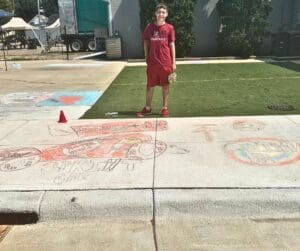 Boy in red shirt smiles at chalk drawing.